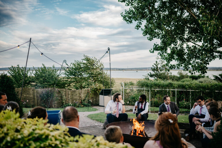 Guests gather around a firepit in a wedding venue garden overlooking the Kent estuary