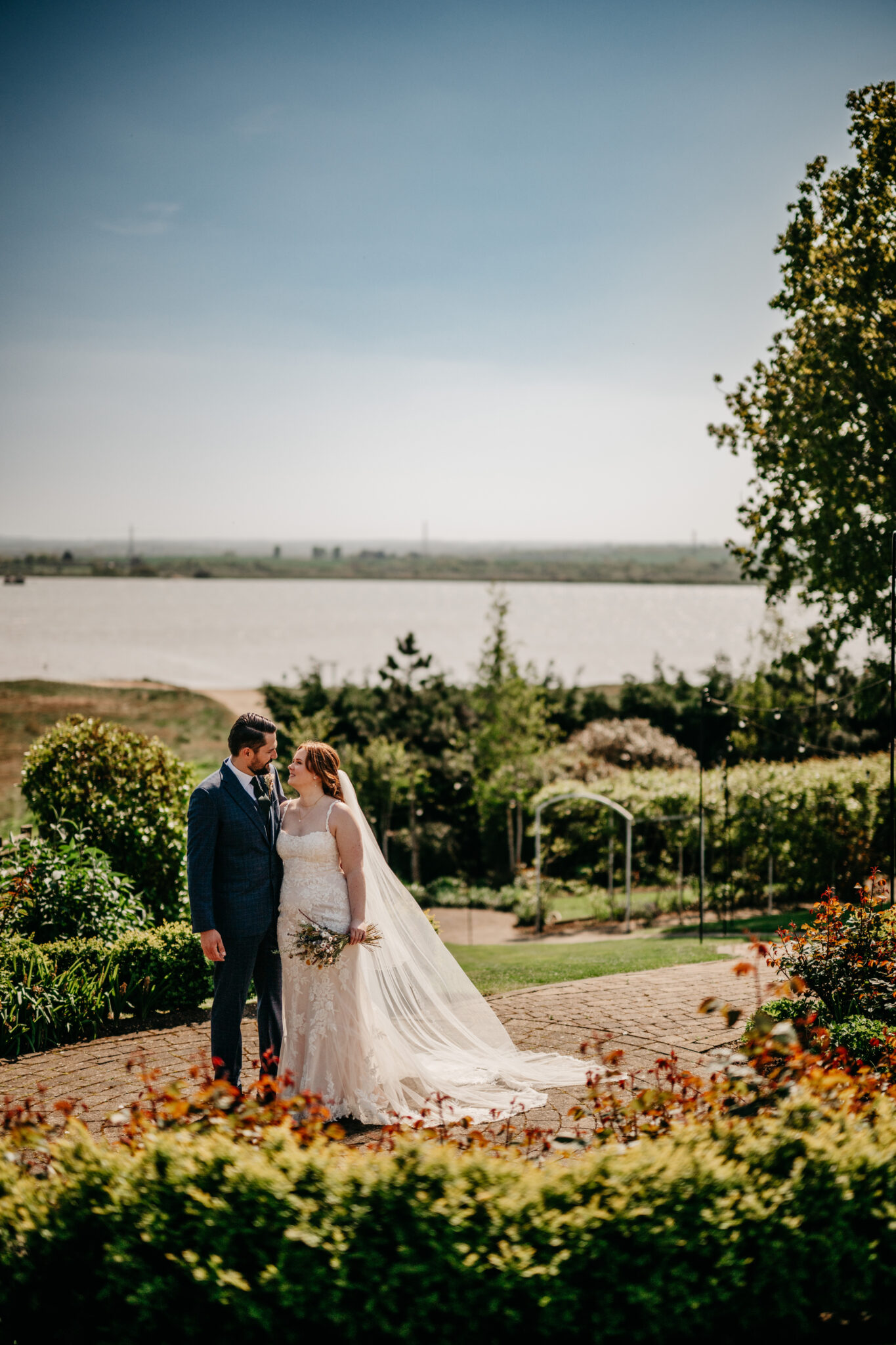 Wedding couple stand in a blooming garden overlooking the estuary in Kent