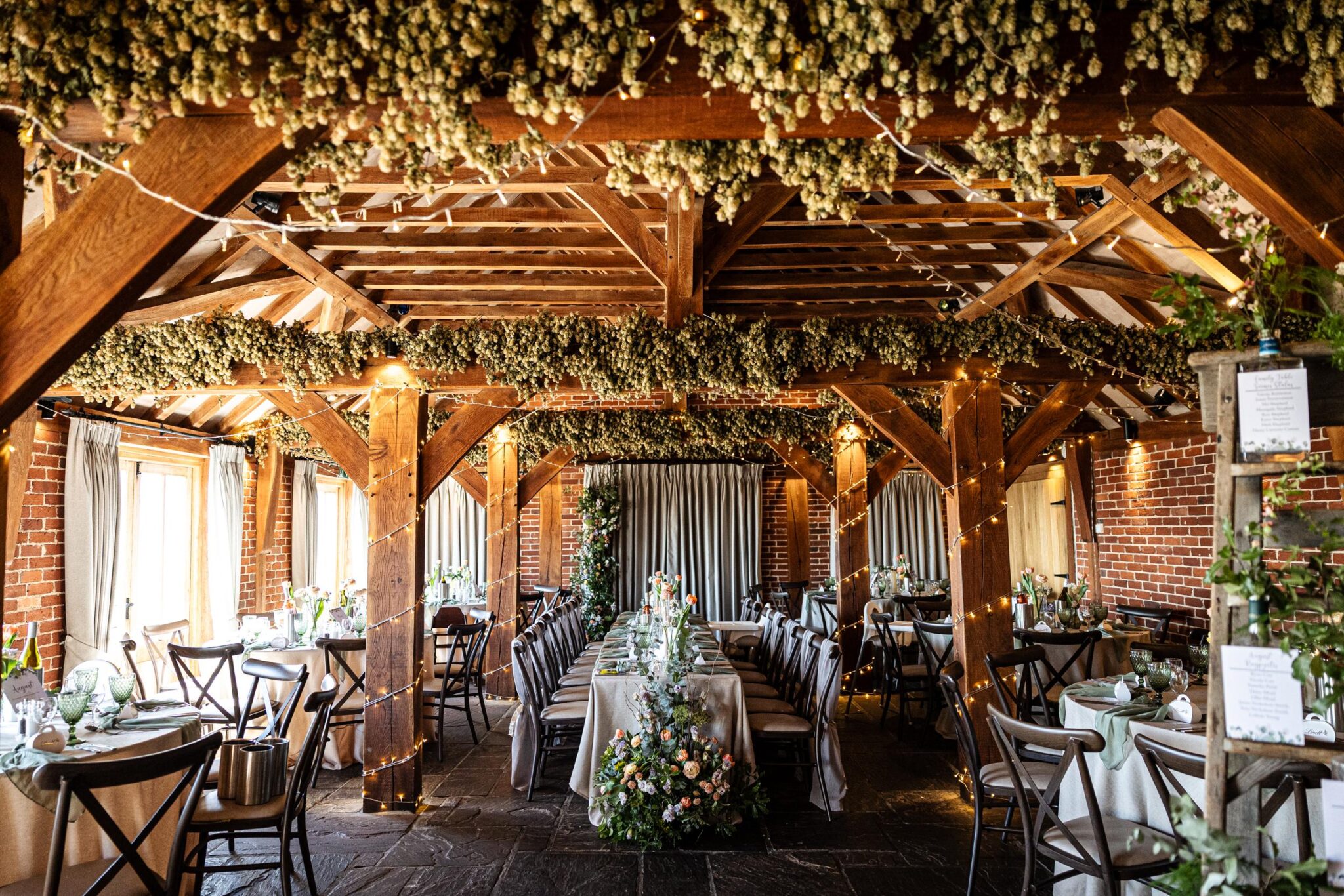 Kent barn wedding breakfast featuring a long central top table and large floral arrangements