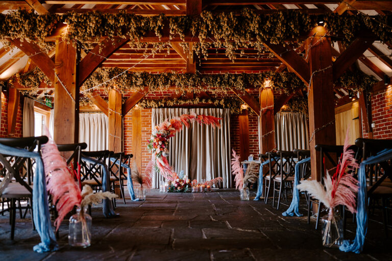 Barn wedding ceremony styled with bold pink florals and feathers