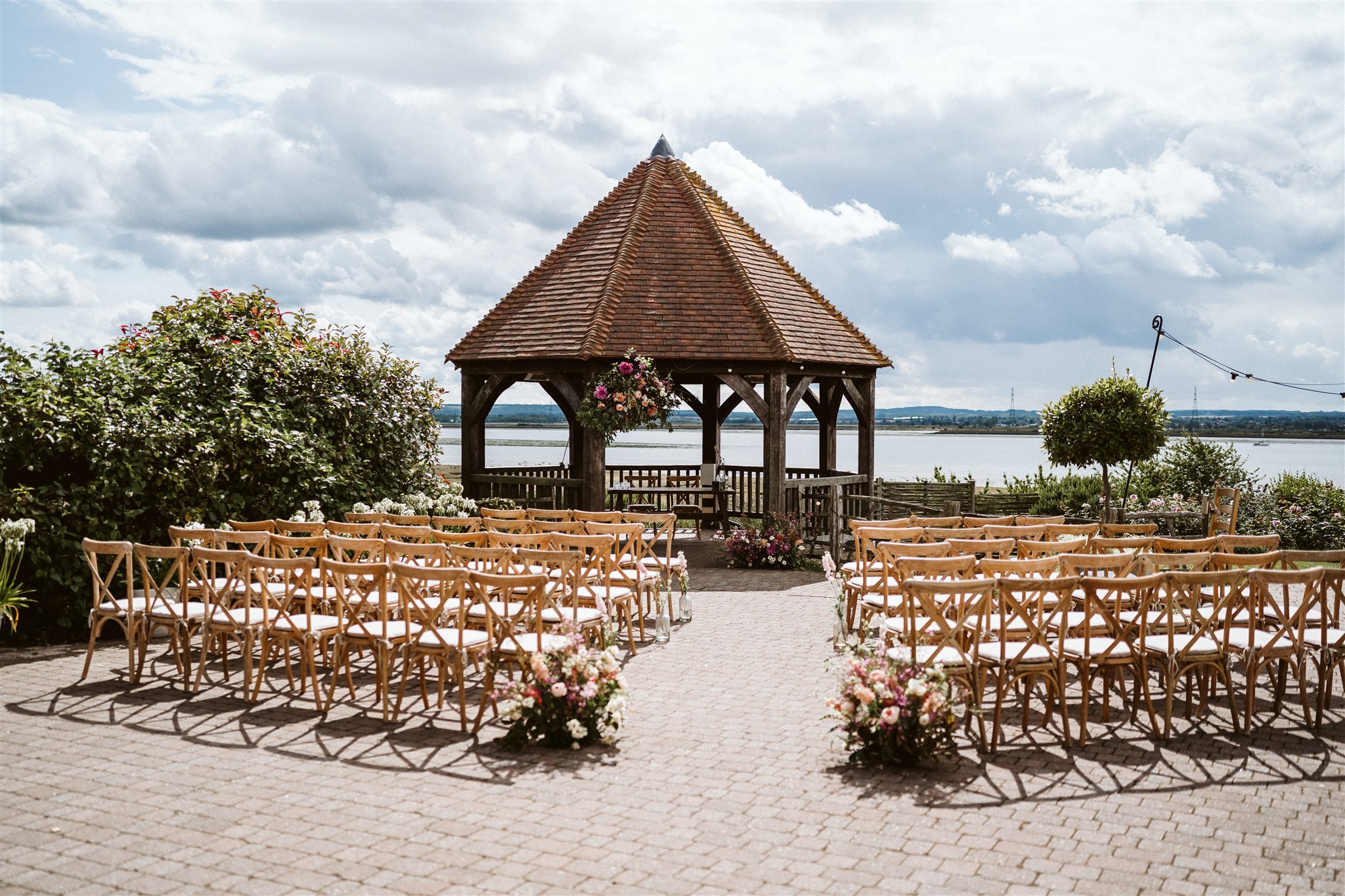 Waterside outdoor wedding ceremony with a wooden gazebo and large flower arrangements