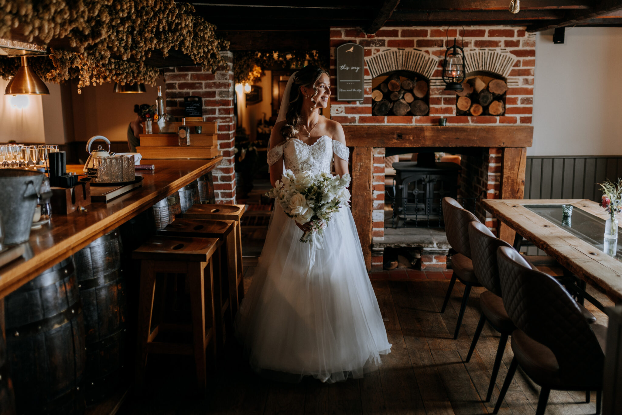 Bride smiles as she walks through a period private wedding pub with log burner and hops