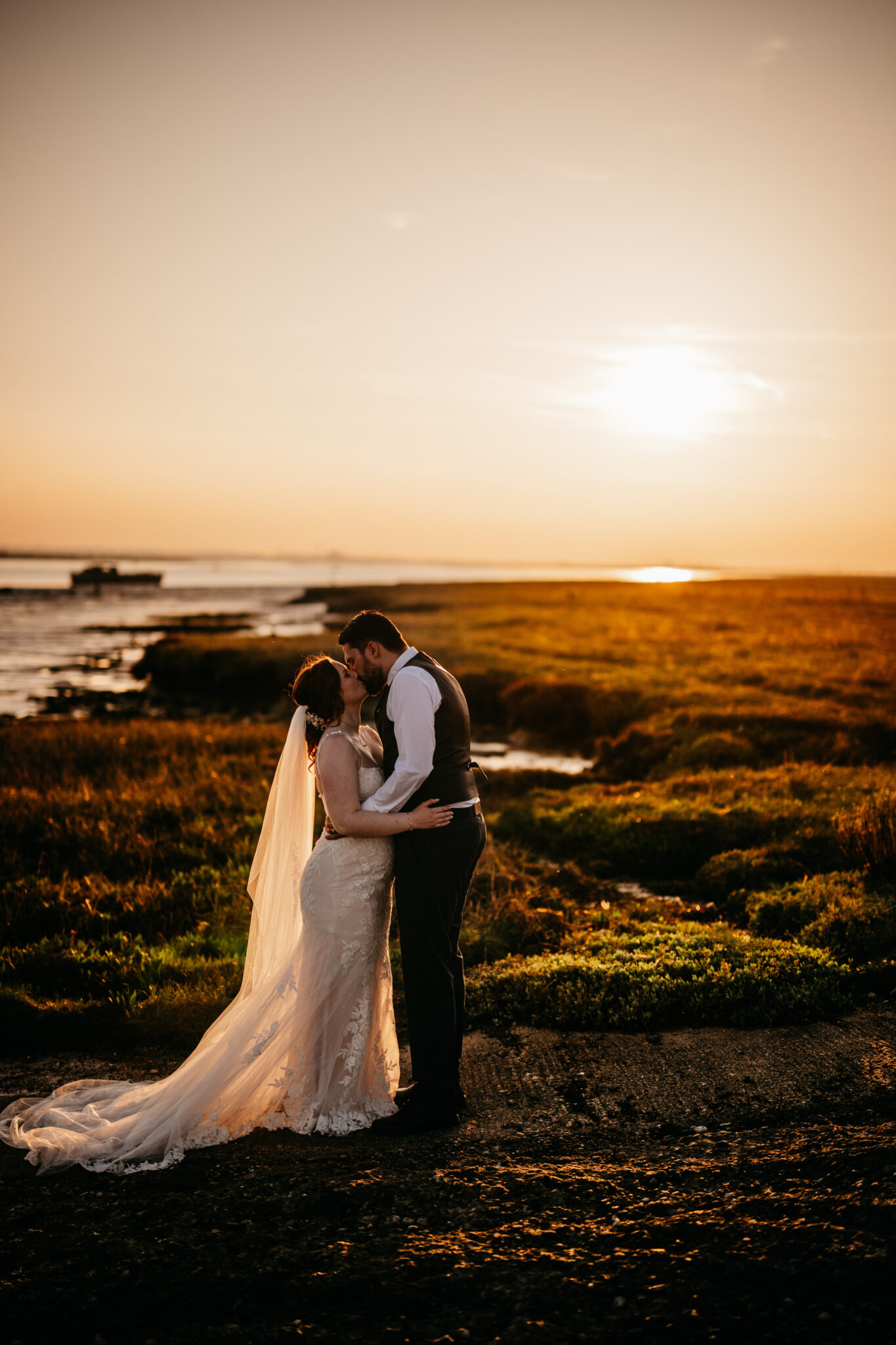 Bride and groom kiss by the Kent estuary at sunset