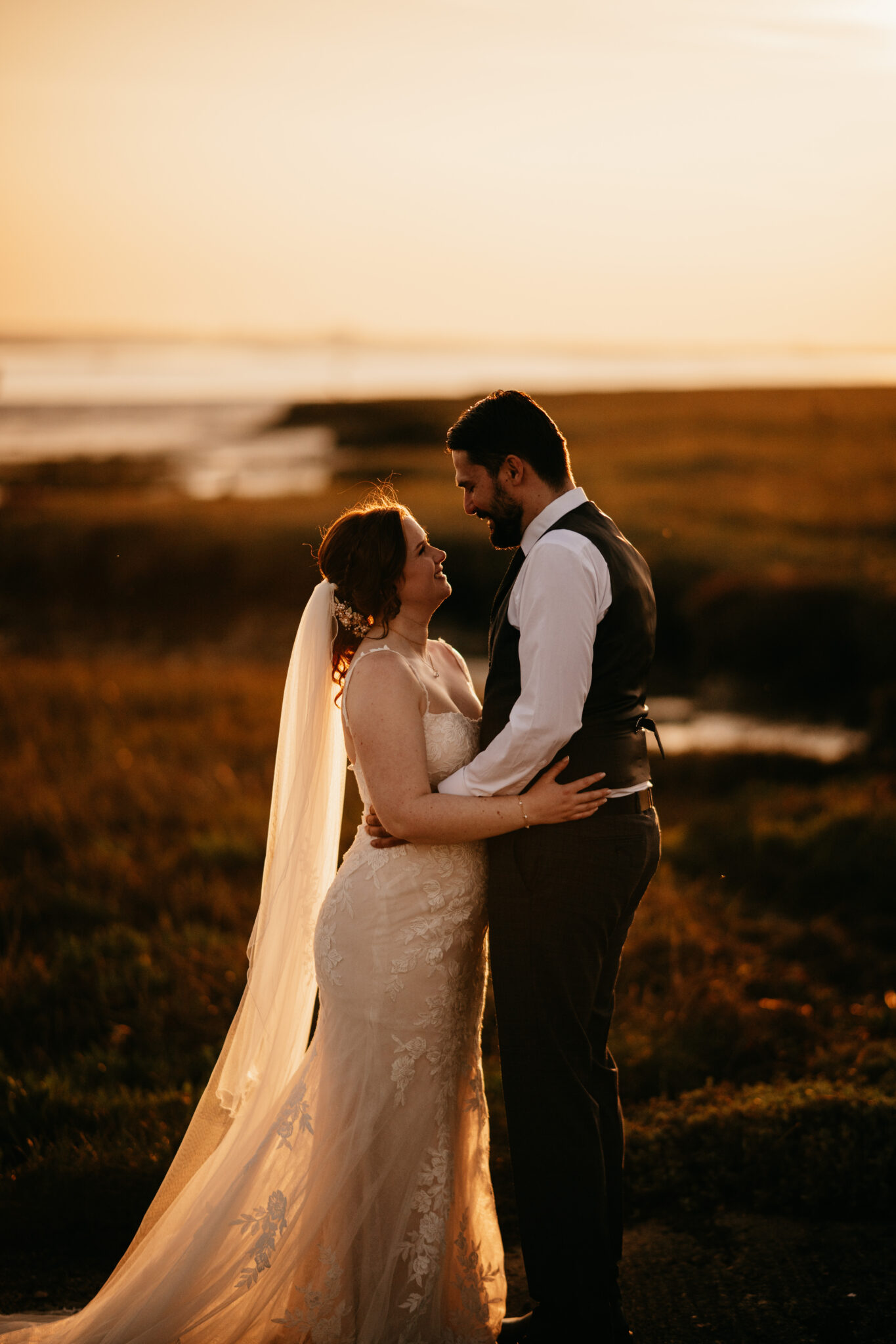 Newlyweds embrace at dusk beside the water at a barn wedding venue in Kent