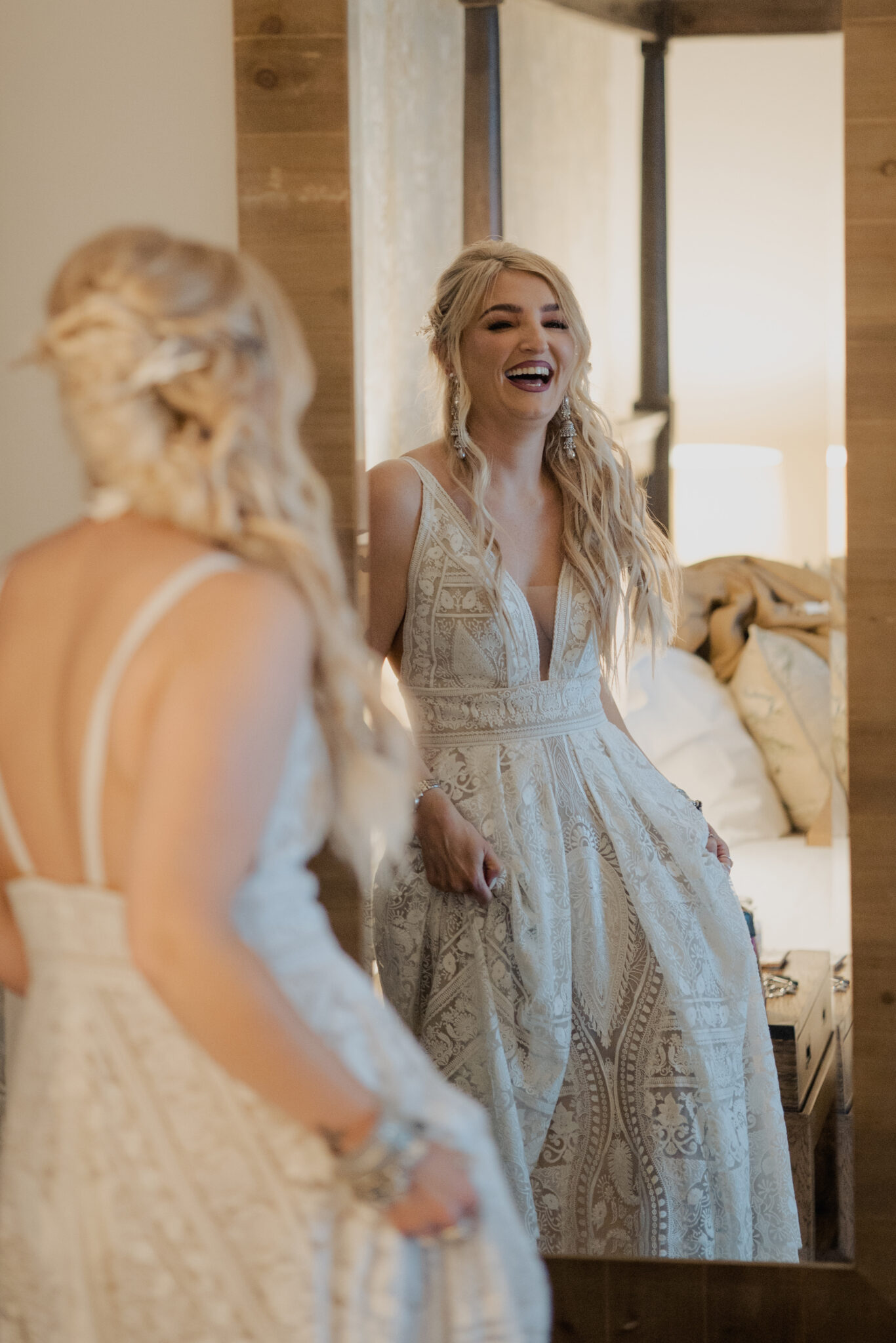 Bride in a vintage lace dress laughs as she admires her reflection in her wedding accommodation mirror