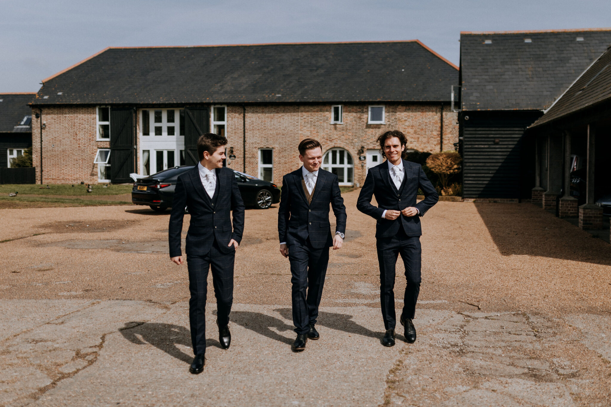 Smart groomsmen walking with their wedding cottage accommodation in the background