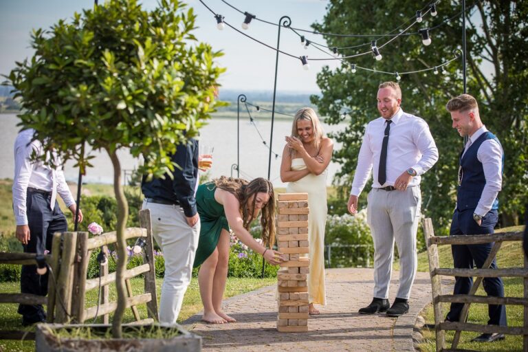 Guests play a wooden tower game in the garden of a barn wedding venue with estuary views