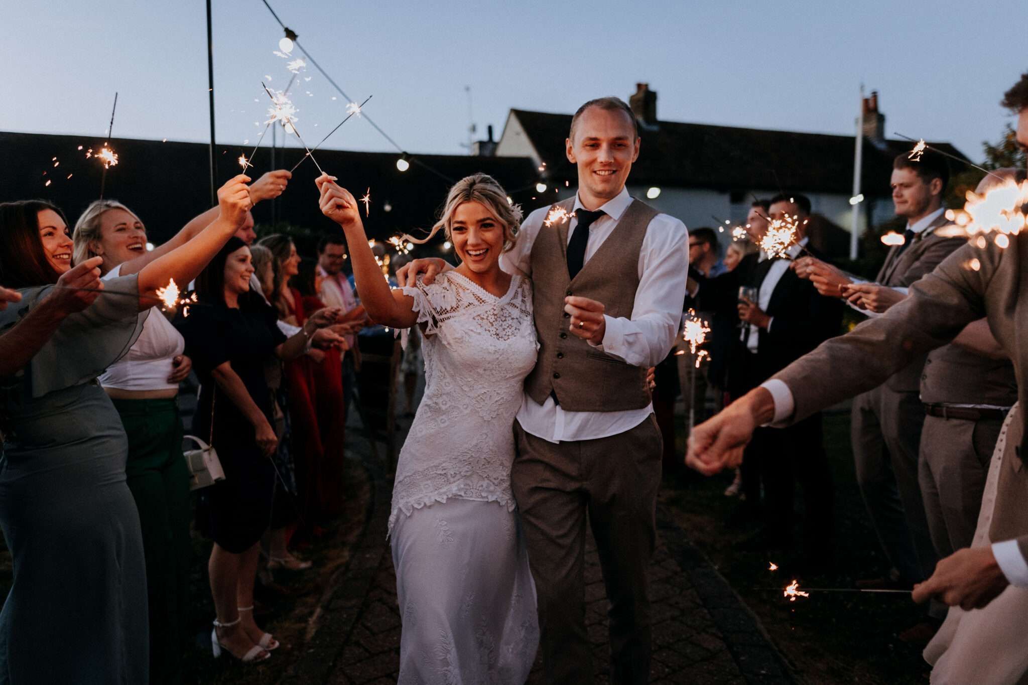 Couple laughing and waving sparklers with guests outside a barn wedding venue