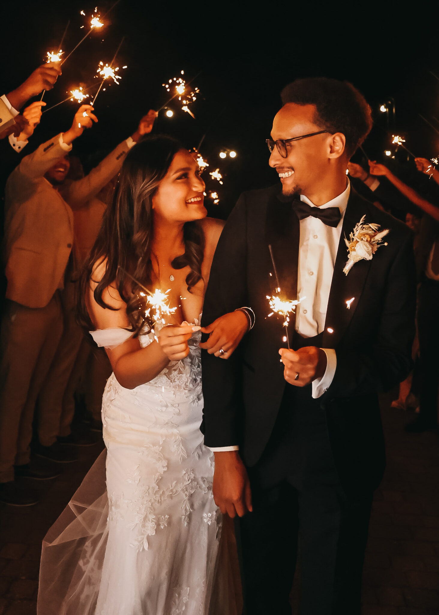 Smiling wedding couple walk beneath an arch of guests holding sparklers