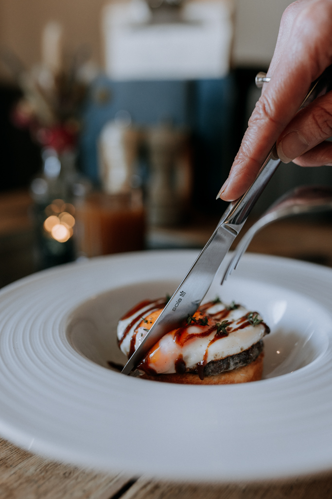 A knife cutting into a fried egg and sausage muffin breakfast