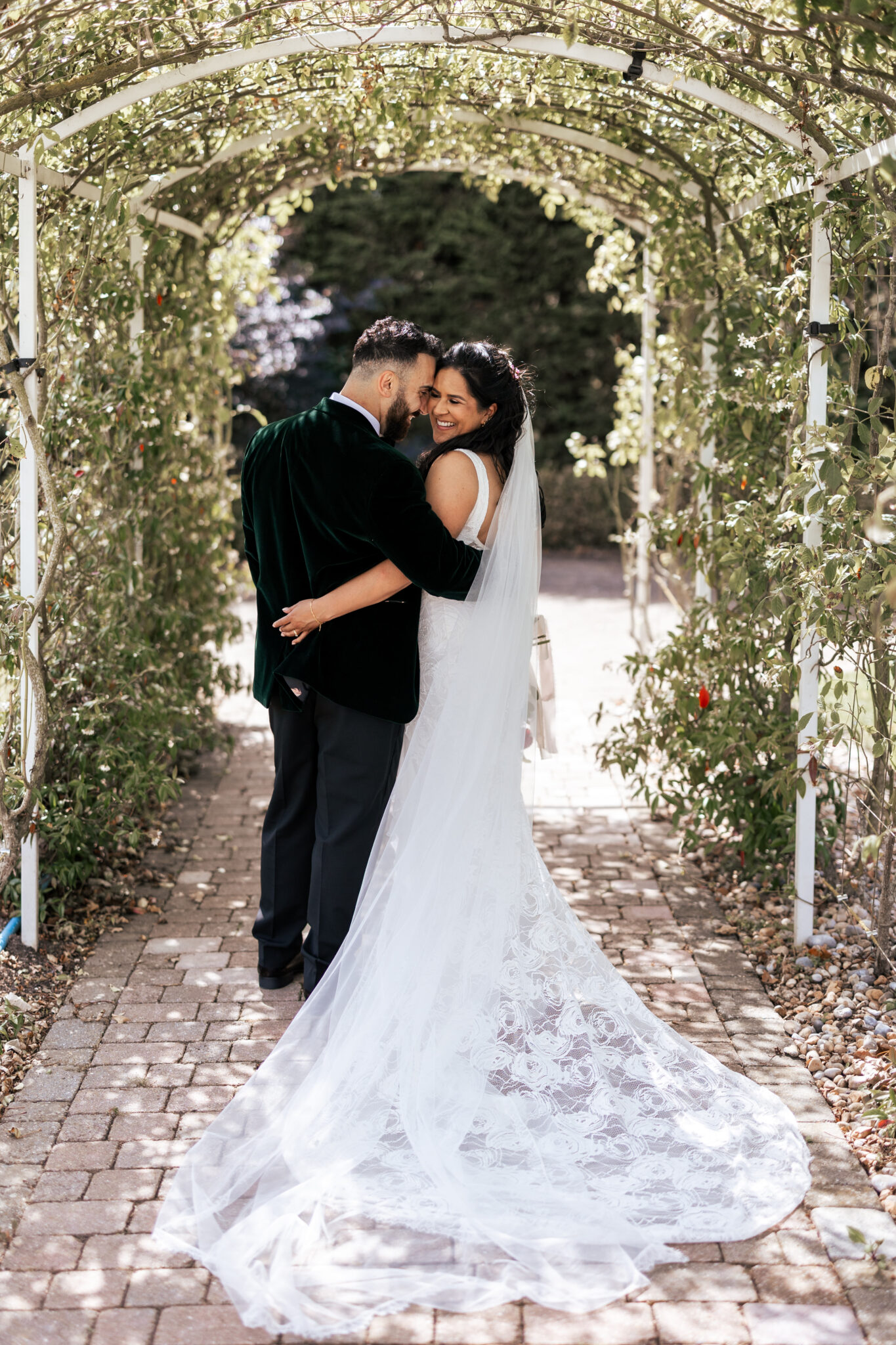 Newlyweds embrace and laugh beneath a rose arch on their wedding day