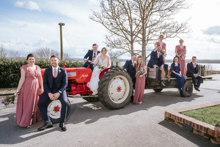 Wedding party posing on a red vintage tractor with trailor and hay bales