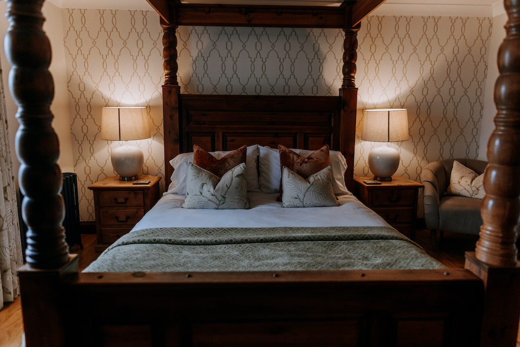 Headboard view of a four poster bed with bedside lamps at a barn wedding venue with accommodation