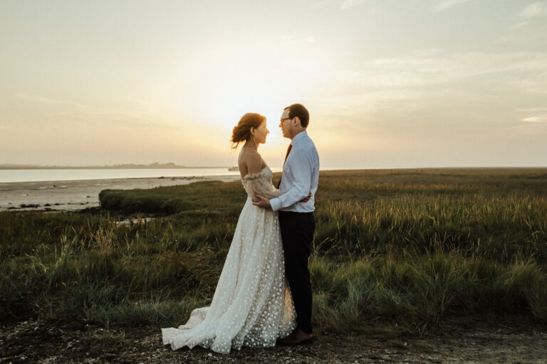 Newlyweds share a tender moment in front of Kent estuary in a meadow at twilight