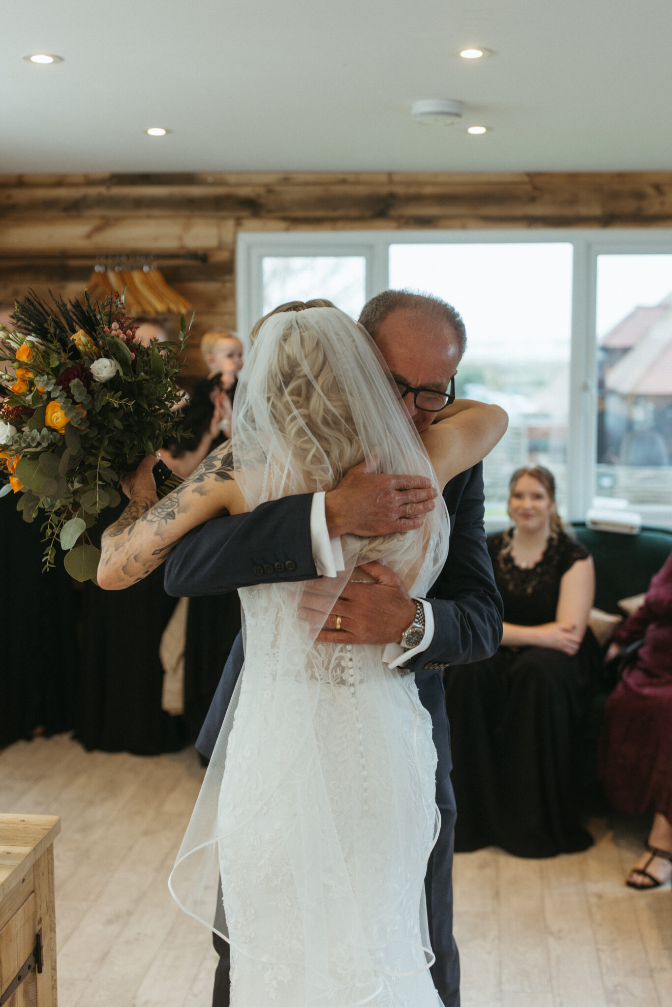 Bride holding bouquet is hugged by her father in a wedding venue getting ready room