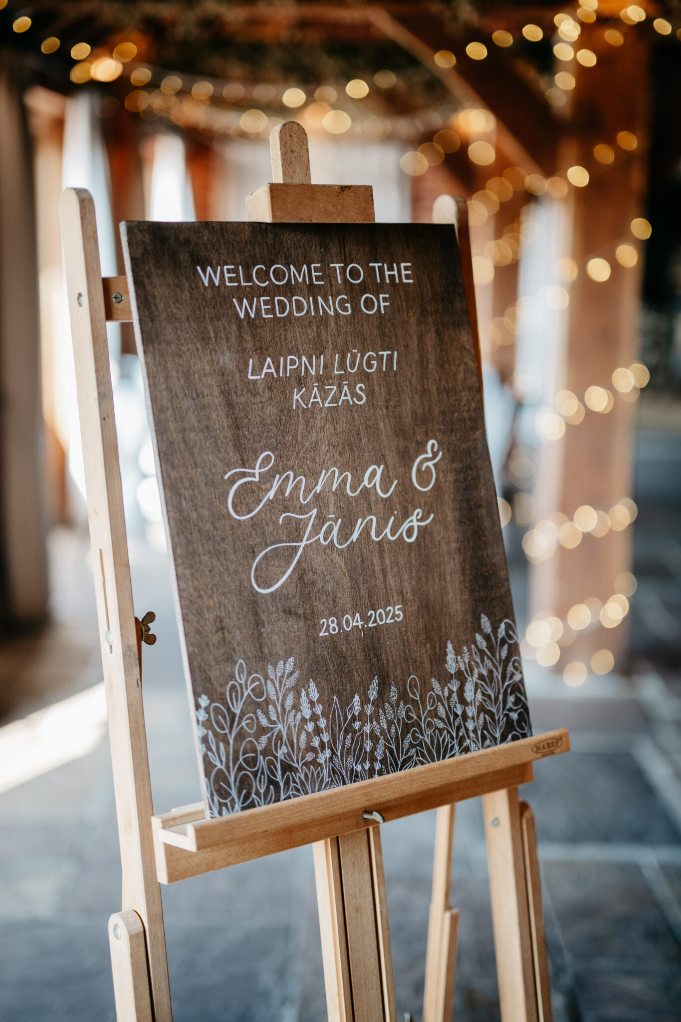 Rustic wedding sign set on a vintage easel in a fairy lit wedding barn