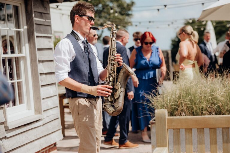 Kent wedding saxophonist entertains guests outdoors during a sunny barn wedding