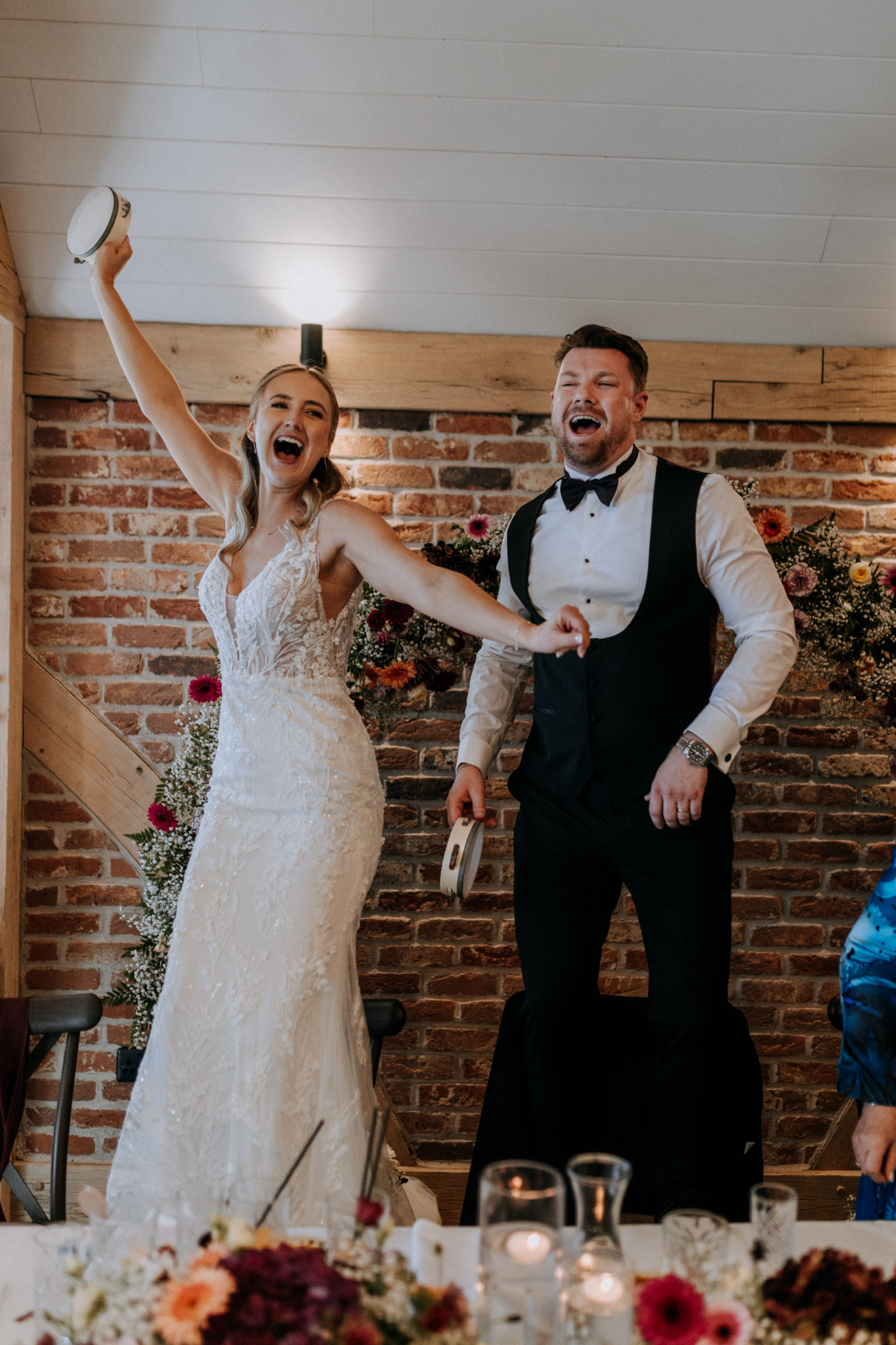 Newlyweds dancing on chairs with a tamborine in a Kent wedding barn