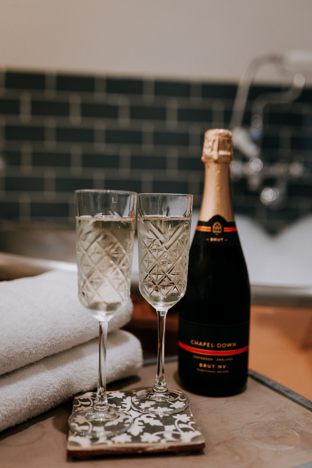 Two glasses and a bottle of sparkling Chapel Down wine in front of a copper bath filled with bubbles