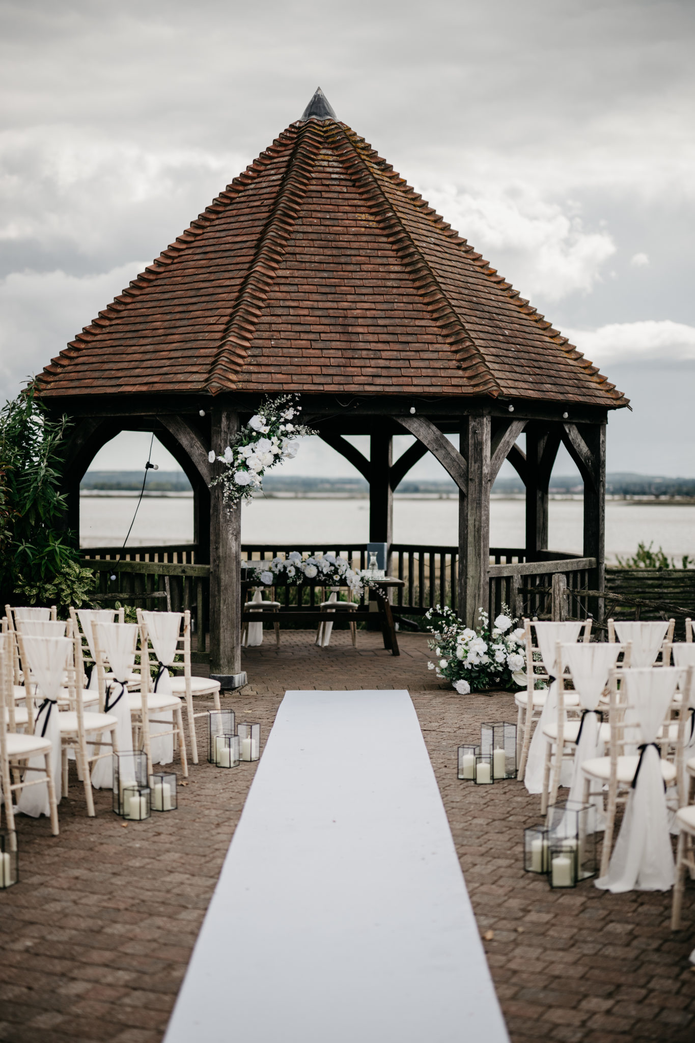 An outdoor wedding ceremony overlooking the water, with a gazebo and white carpet aisle and styling