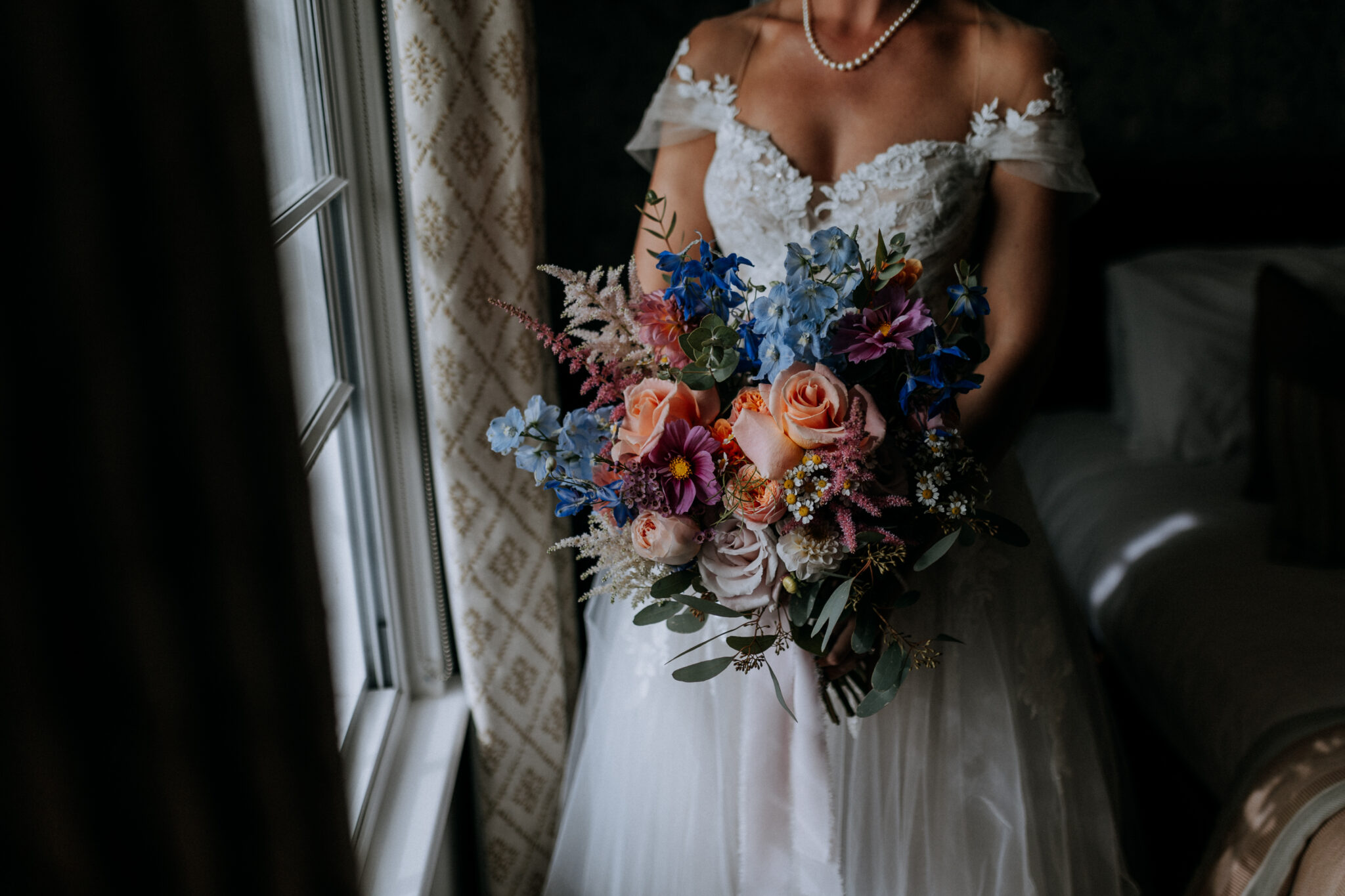 A bride standing by a window holding a bouquet of colourful spring flowers