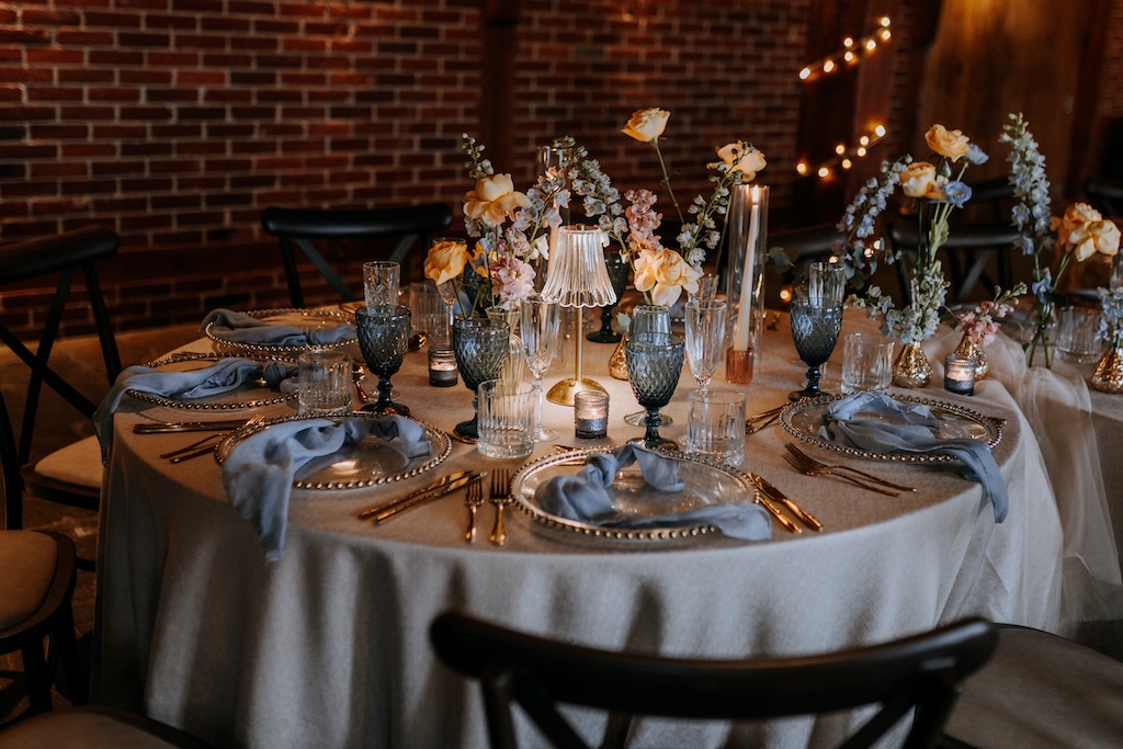 A wedding breakfast table set to a blue spring theme, in a rustic wedding barn