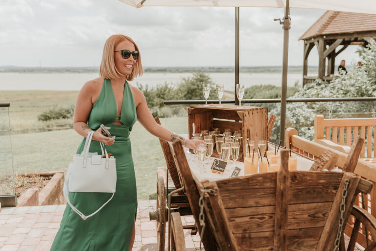 Smiling wedding guest takes a drink from a rustic waterside drinks cart