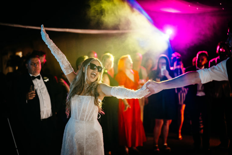 Bride in sunglasses and long sleeved gloves dances during her wedding party