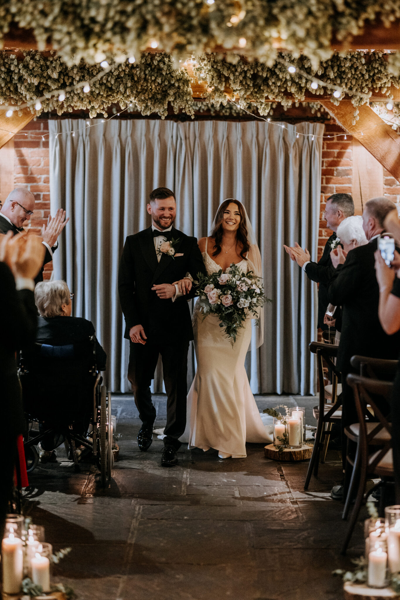 Newlyweds at the end of a candle lit aisle in a wedding barn
