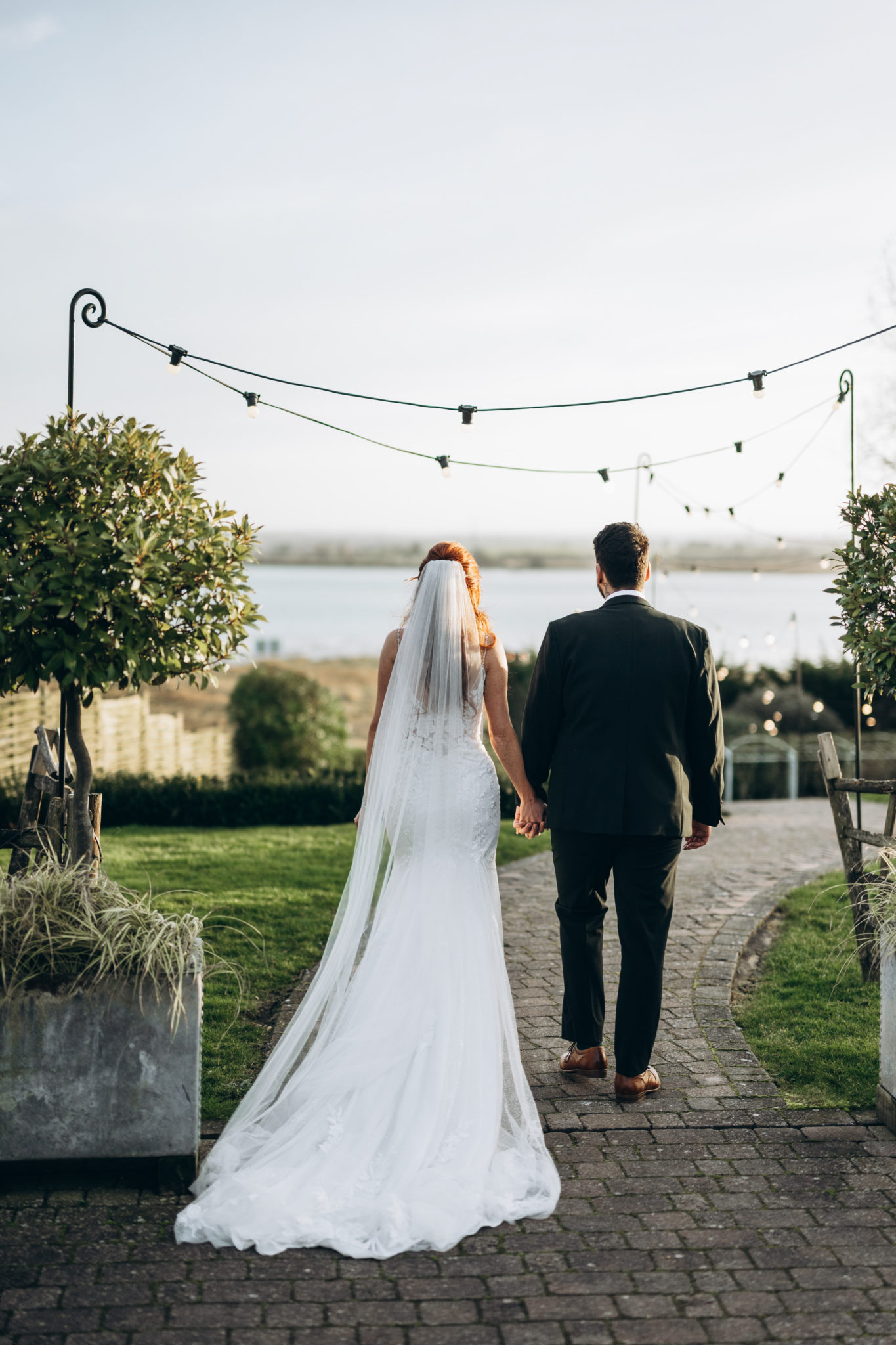 Newlyweds stand back to the camera, in a wedding garden overlooking the Kent estuary