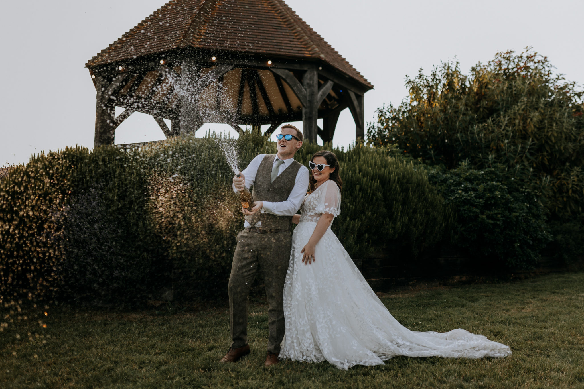 Newlyweds in sunglasses spray champagne on their wedding day