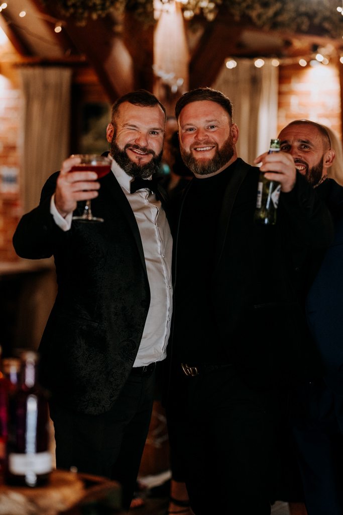 Two suited men wink and raise drinks during a Christmas party