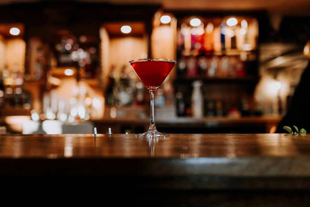 Red martini style cocktail stands on a wooden bar during a Christmas party
