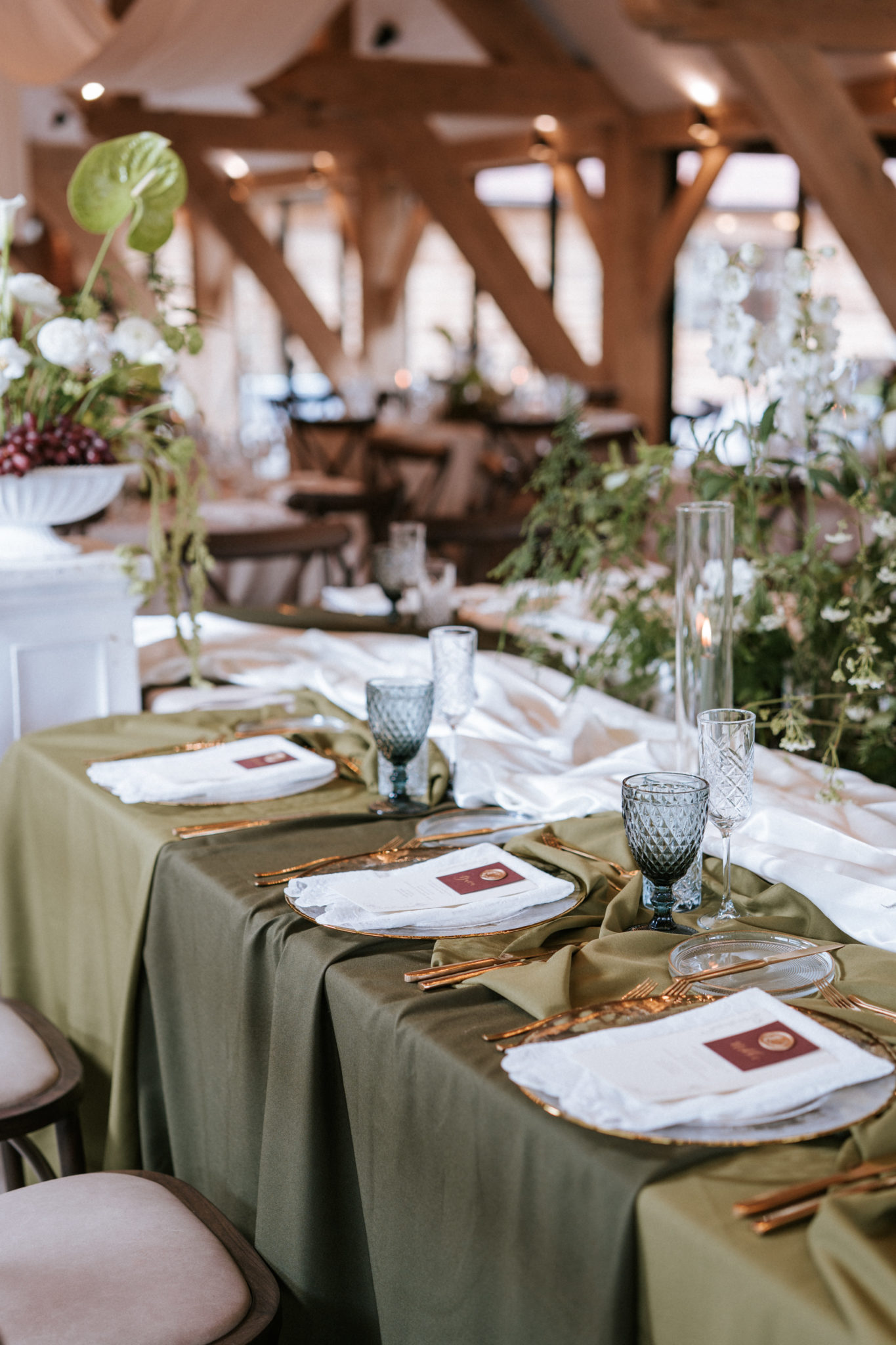 Styled barn wedding breakfast table with green layered cloths and elegant tablewear