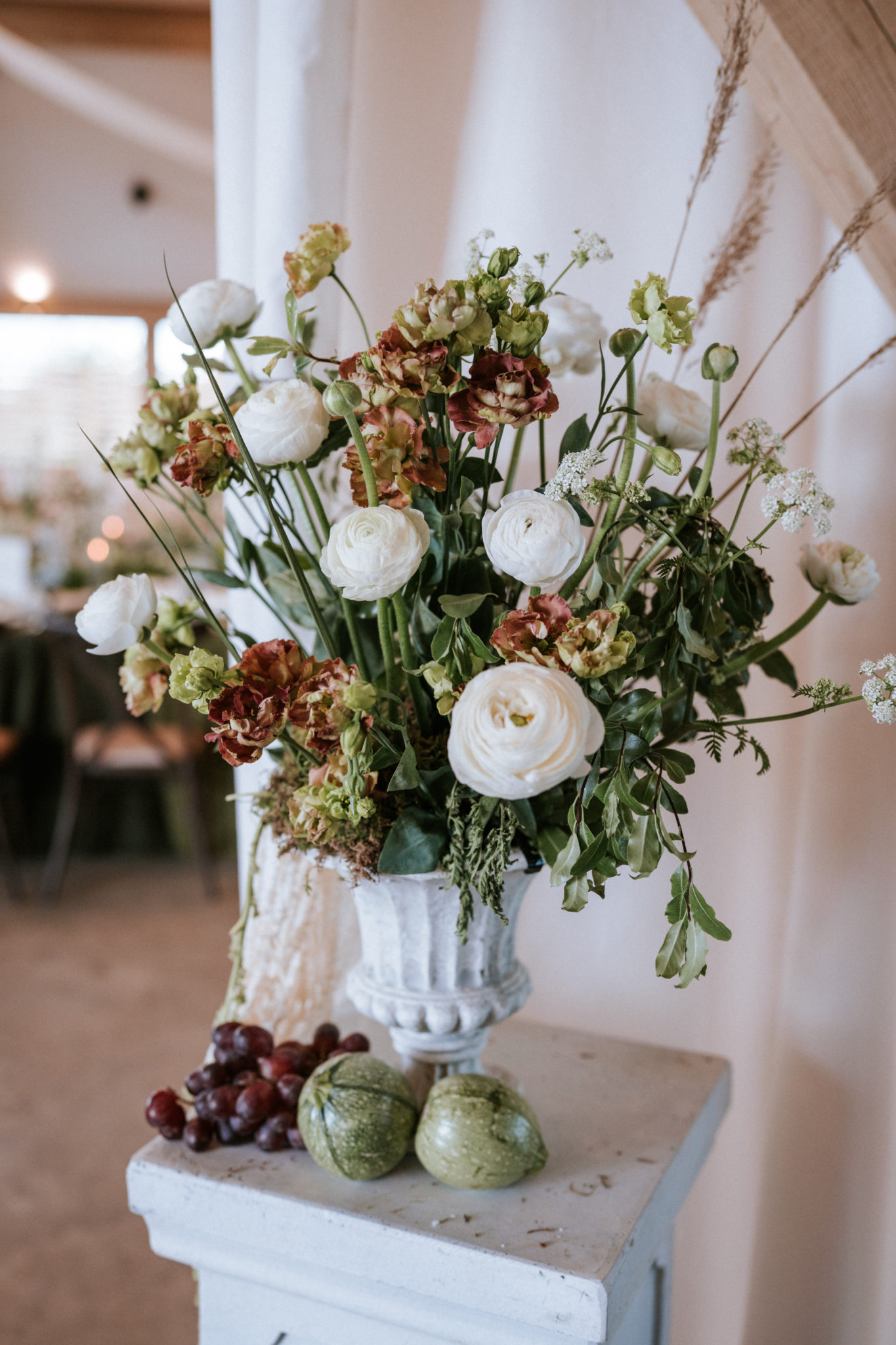 White plinth decorated with flowers, foliage and fruit for a barn wedding